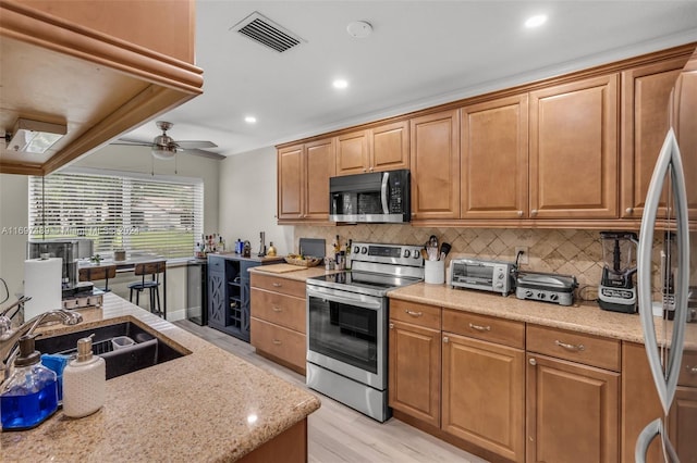 kitchen with stainless steel appliances, light wood-type flooring, ceiling fan, decorative backsplash, and sink