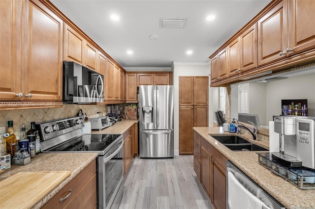 kitchen with sink, light hardwood / wood-style floors, backsplash, light stone countertops, and appliances with stainless steel finishes