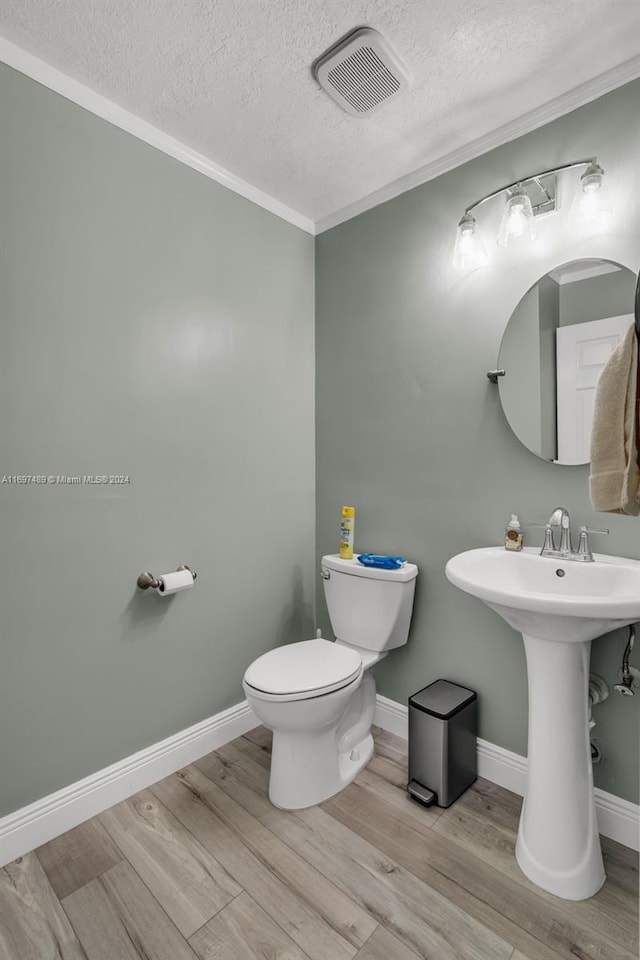 bathroom with toilet, hardwood / wood-style flooring, a textured ceiling, and crown molding