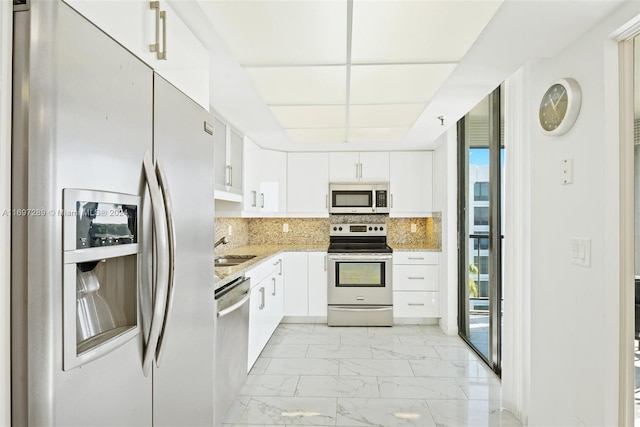 kitchen with white cabinets, backsplash, light stone countertops, and stainless steel appliances