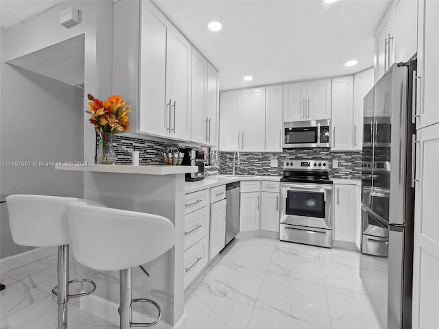 kitchen with a kitchen bar, appliances with stainless steel finishes, backsplash, and white cabinets