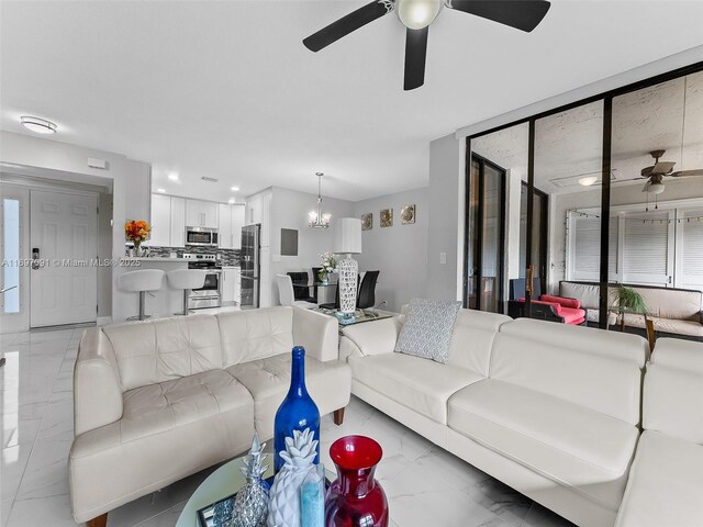 living room with ceiling fan with notable chandelier, recessed lighting, and marble finish floor