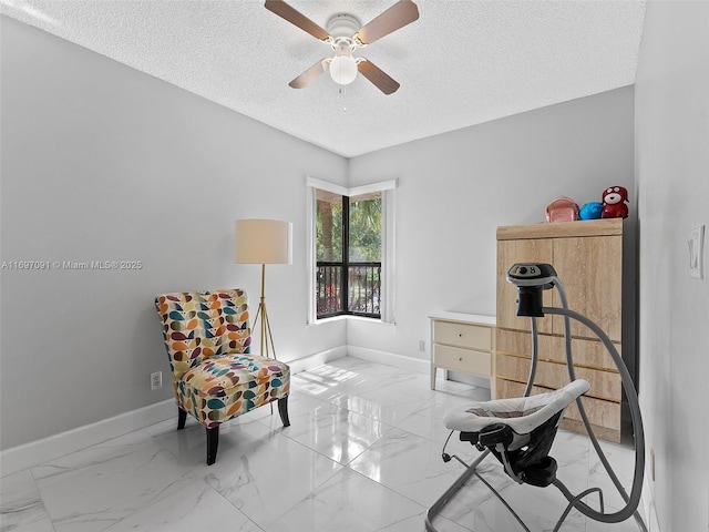 sitting room featuring baseboards, ceiling fan, a textured ceiling, and marble finish floor