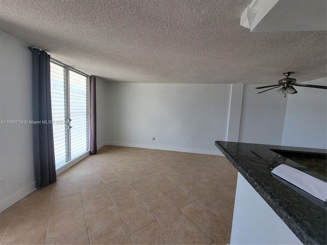 unfurnished living room featuring light tile patterned floors, a ceiling fan, baseboards, and a textured ceiling