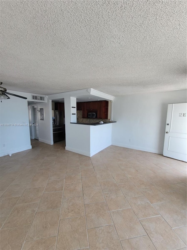 unfurnished living room with a ceiling fan, a fireplace with raised hearth, visible vents, and a textured ceiling