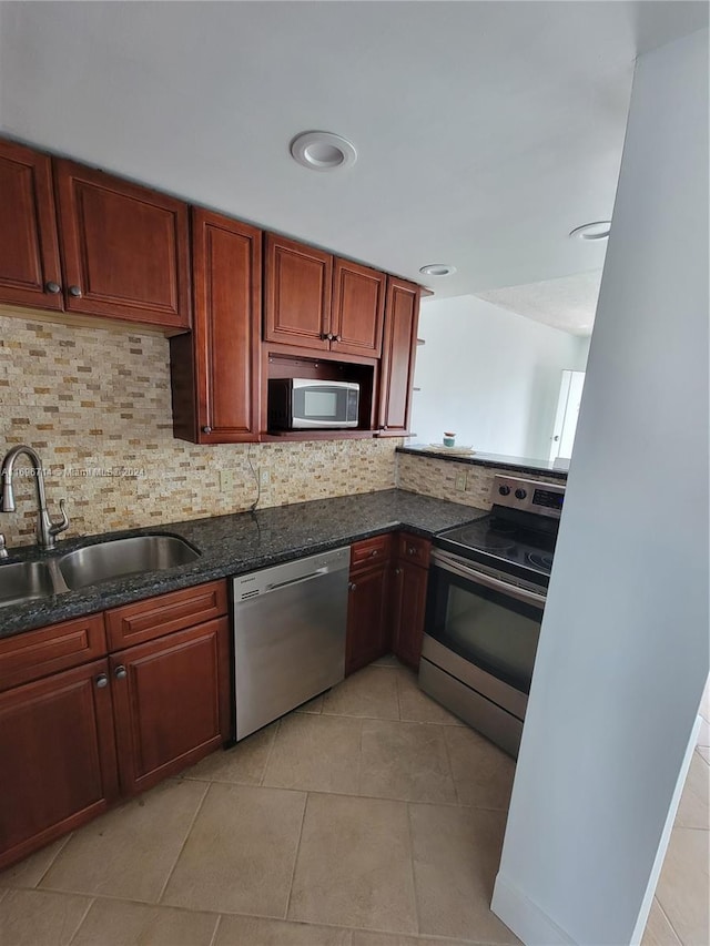 kitchen featuring light tile patterned floors, dark stone counters, a sink, decorative backsplash, and stainless steel appliances