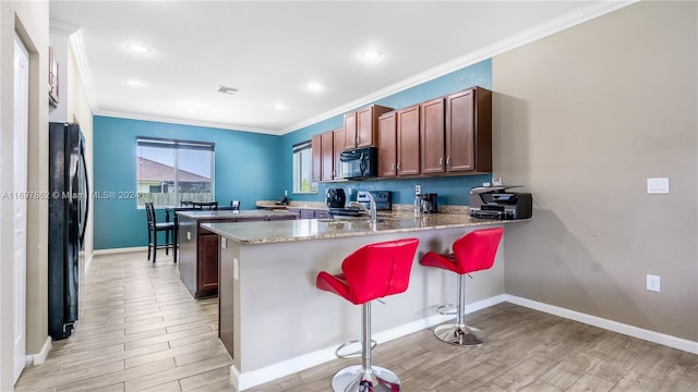 kitchen featuring black appliances, a kitchen breakfast bar, light hardwood / wood-style floors, and kitchen peninsula