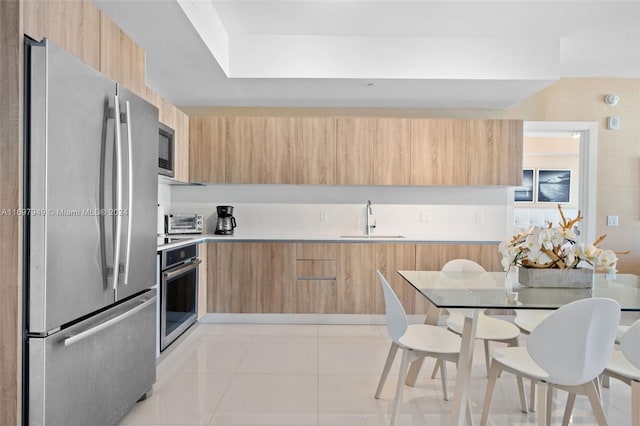 kitchen with sink, light tile patterned floors, stainless steel appliances, and light brown cabinets