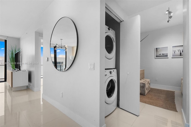 clothes washing area featuring an inviting chandelier, stacked washer / dryer, and light tile patterned flooring