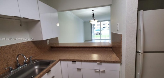 kitchen featuring decorative backsplash, sink, pendant lighting, white refrigerator, and white cabinets