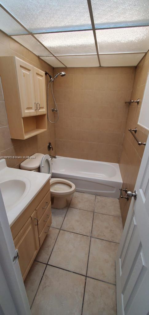 full bathroom featuring tile patterned flooring, vanity, tiled shower / bath combo, and toilet