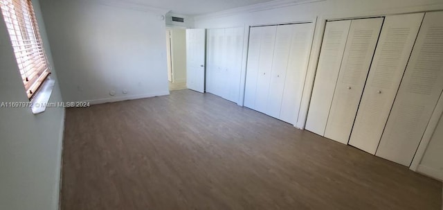 unfurnished bedroom with multiple closets, dark hardwood / wood-style floors, and ornamental molding