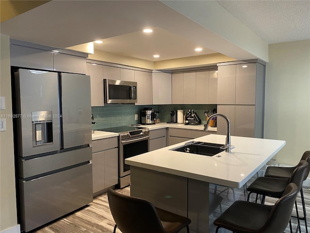 kitchen featuring sink, backsplash, a breakfast bar, appliances with stainless steel finishes, and light wood-type flooring