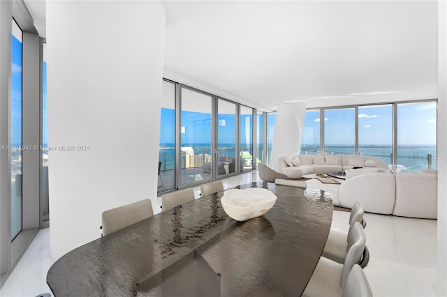 dining area with light tile patterned floors, a water view, and a wall of windows