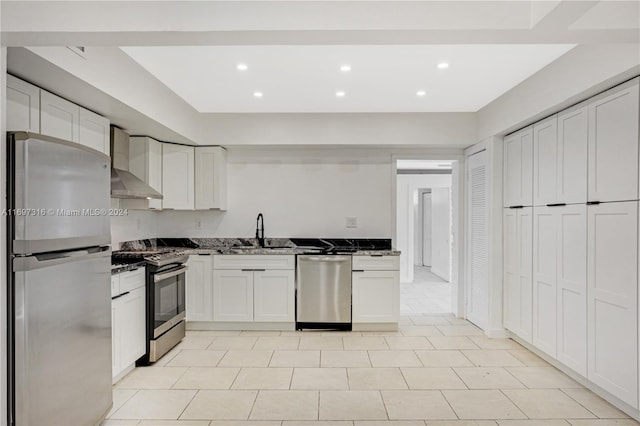 kitchen featuring sink, stainless steel appliances, wall chimney range hood, dark stone counters, and white cabinets