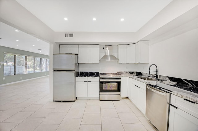 kitchen featuring white cabinetry, sink, wall chimney range hood, dark stone countertops, and appliances with stainless steel finishes