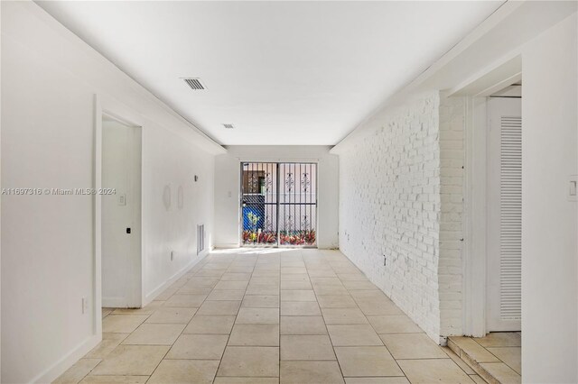 unfurnished room with light tile patterned flooring and brick wall