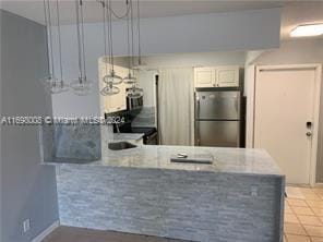 kitchen featuring kitchen peninsula, light tile patterned floors, black range, white cabinets, and stainless steel refrigerator