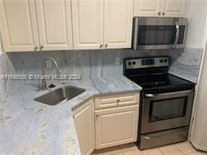 kitchen with sink, light tile patterned floors, appliances with stainless steel finishes, tasteful backsplash, and light stone counters