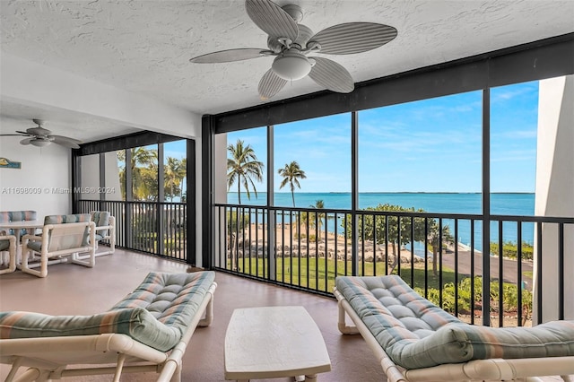 sunroom featuring ceiling fan and a water view