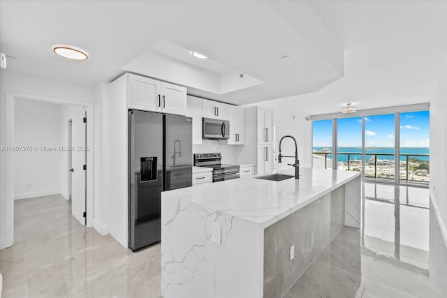 kitchen featuring a wall of windows, sink, appliances with stainless steel finishes, a water view, and white cabinets