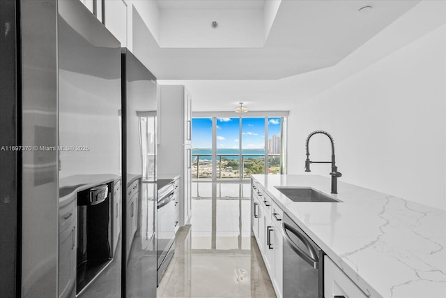 kitchen featuring dishwasher, sink, white cabinetry, a wall of windows, and light stone counters