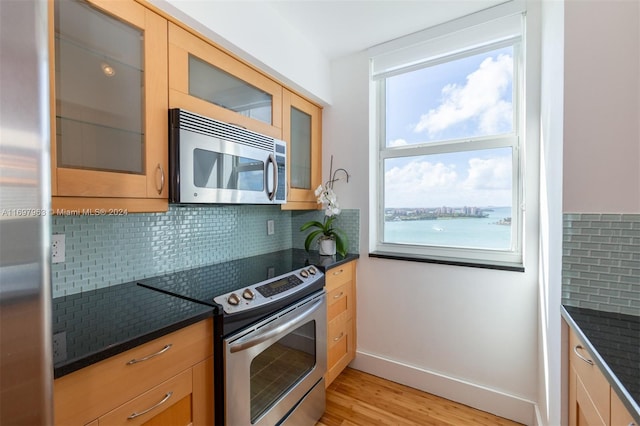 kitchen featuring backsplash, light hardwood / wood-style flooring, a water view, and appliances with stainless steel finishes