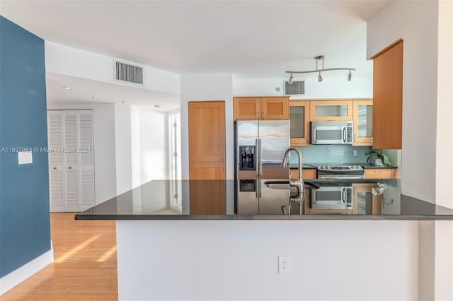 kitchen featuring kitchen peninsula, appliances with stainless steel finishes, decorative backsplash, sink, and light hardwood / wood-style flooring