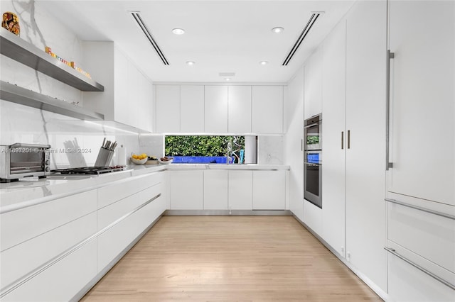 kitchen featuring stainless steel gas cooktop, white cabinetry, sink, and light wood-type flooring