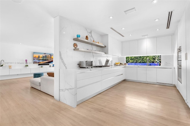 kitchen with tasteful backsplash, light hardwood / wood-style flooring, and white cabinets