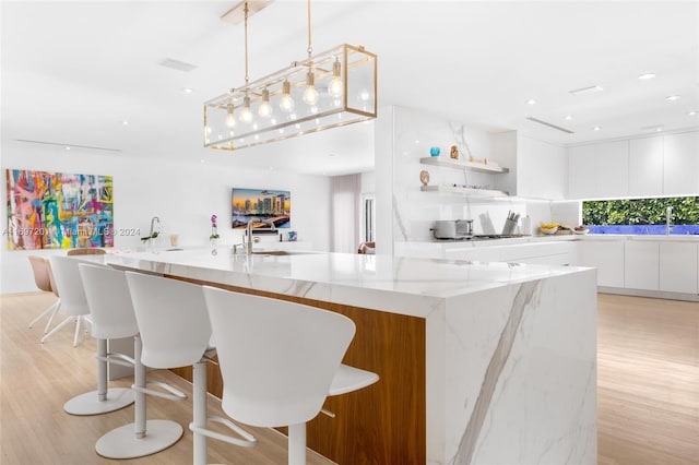 kitchen with white cabinets, light hardwood / wood-style floors, light stone counters, and hanging light fixtures