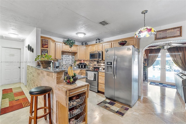 kitchen with kitchen peninsula, appliances with stainless steel finishes, decorative backsplash, a kitchen breakfast bar, and dark stone counters