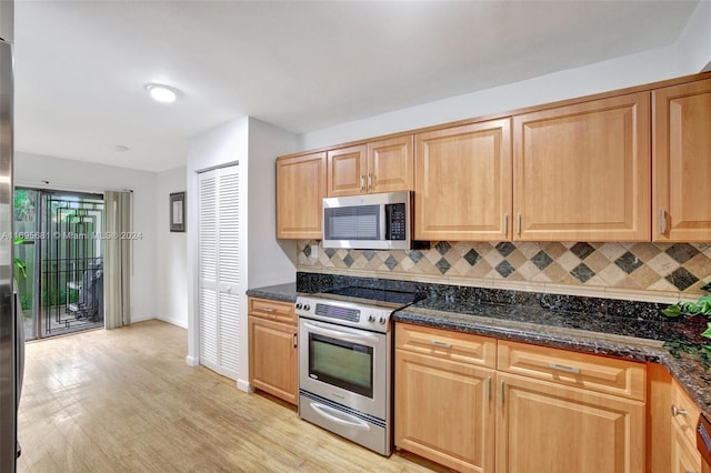 kitchen with stainless steel appliances, light hardwood / wood-style flooring, and dark stone countertops