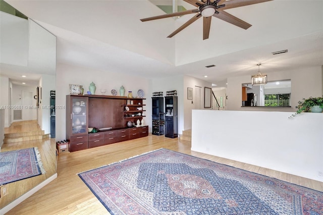 living room featuring ceiling fan with notable chandelier, a towering ceiling, and light hardwood / wood-style flooring