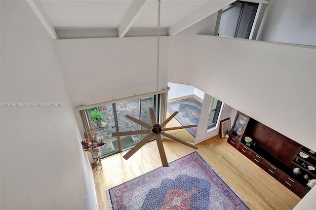 living room with beamed ceiling, wood-type flooring, a towering ceiling, and ceiling fan