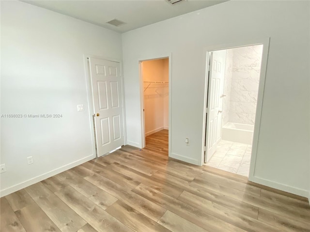 unfurnished bedroom with ensuite bathroom, a closet, a spacious closet, and light hardwood / wood-style flooring