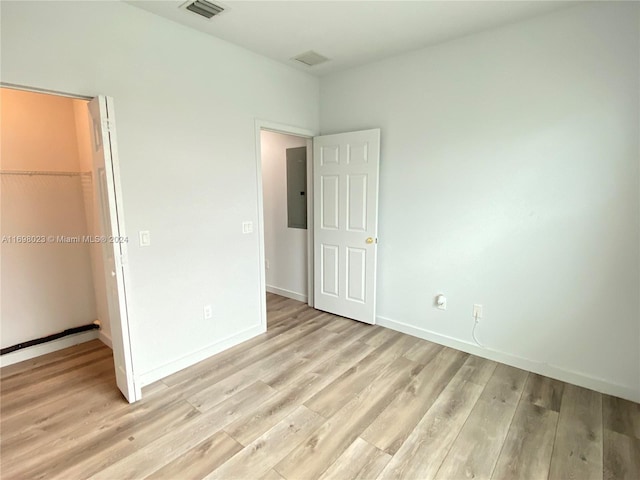 unfurnished bedroom featuring a closet, a spacious closet, electric panel, and light hardwood / wood-style flooring