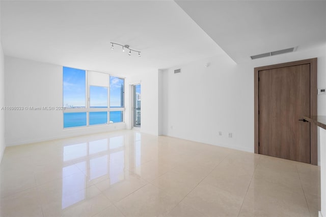 tiled empty room featuring a water view and track lighting