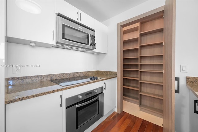 kitchen with dark stone counters, white cabinetry, dark wood-type flooring, and appliances with stainless steel finishes