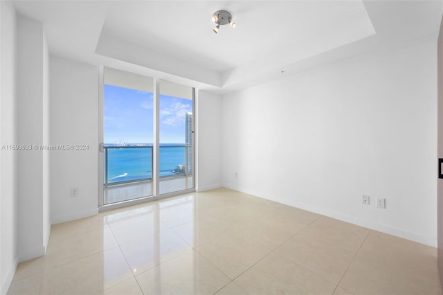 unfurnished room with light tile patterned floors, a water view, a wall of windows, and a tray ceiling