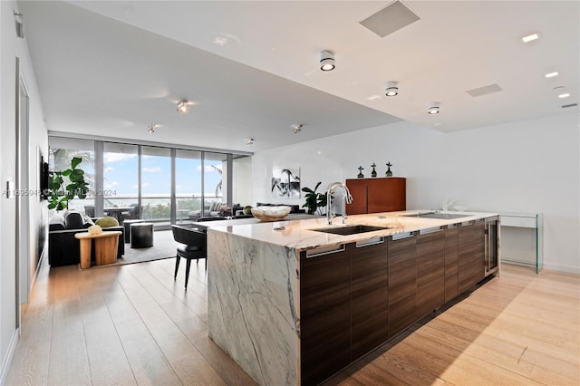 kitchen featuring light hardwood / wood-style floors, light stone counters, sink, and a large island with sink