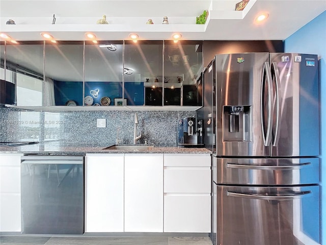 kitchen featuring decorative backsplash, stainless steel appliances, sink, dark stone countertops, and white cabinets