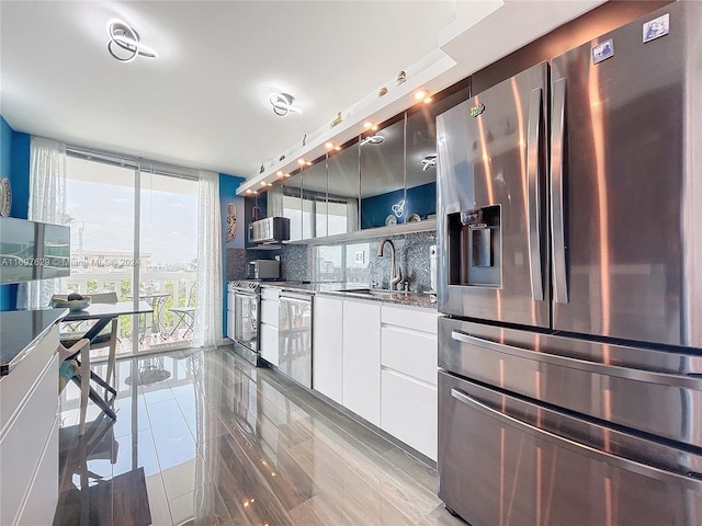 kitchen with appliances with stainless steel finishes, backsplash, floor to ceiling windows, sink, and white cabinets