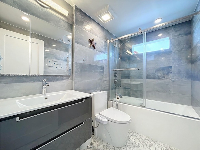 full bathroom with tile patterned flooring, bath / shower combo with glass door, toilet, vanity, and tile walls