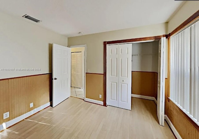 unfurnished bedroom with wood walls, light wood-type flooring, and a closet