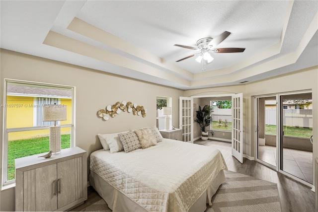 bedroom with dark wood-type flooring, access to outside, french doors, ceiling fan, and a tray ceiling