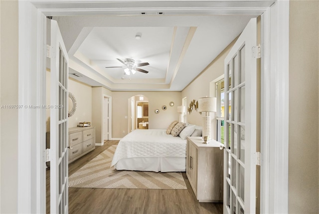 bedroom featuring hardwood / wood-style flooring, ceiling fan, french doors, and a tray ceiling