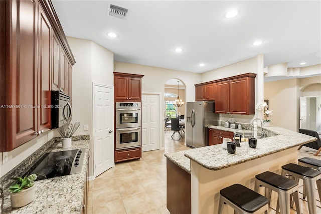 kitchen with a breakfast bar area, kitchen peninsula, light stone countertops, and appliances with stainless steel finishes