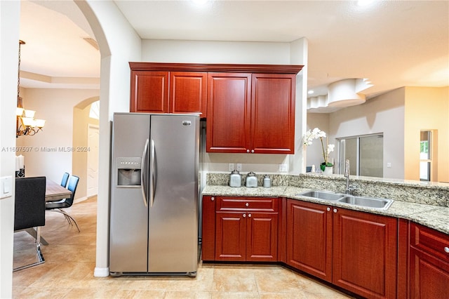 kitchen featuring a chandelier, stainless steel fridge, sink, and light stone counters