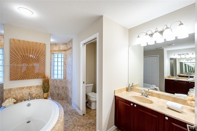 bathroom with tile patterned floors, vanity, a textured ceiling, tiled tub, and toilet